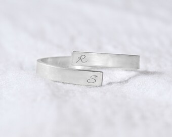 Può includere: Un anello d'argento con una fascia divisa, inciso con le lettere "L" e "S".