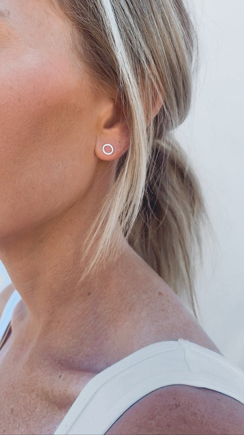 May include: A close-up of a person's ear with a small, silver hoop earring. The earring is simple and minimalist, with a thin, circular design.