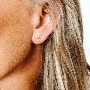 May include: A close-up of a person's ear with a small gold butterfly earring. The earring is a delicate, simple design.