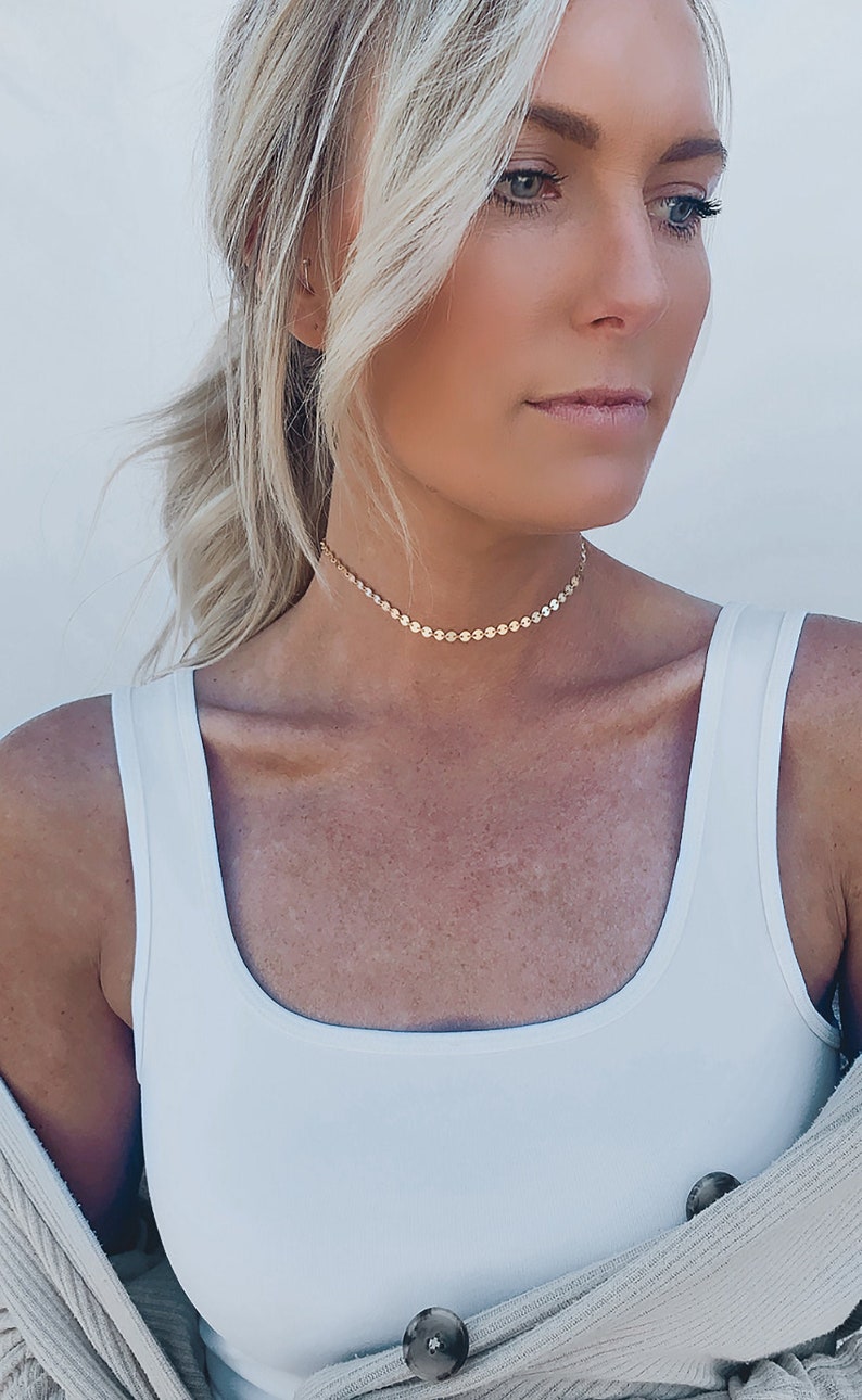 Pode incluir: Uma mulher vestindo um top branco sem mangas e um colar de corrente dourada. O colar &eacute; feito de pequenas contas redondas.