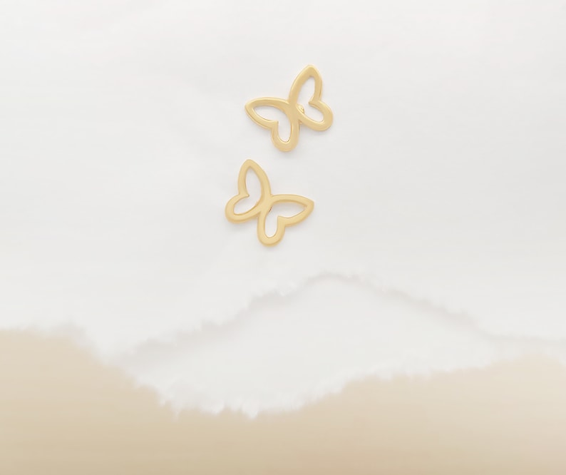 May include: Two gold butterfly shaped earrings on a white background.