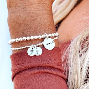 May include: A silver beaded bracelet with two charms. One charm has the word "mama" engraved on it, and the other charm has a small flower design.