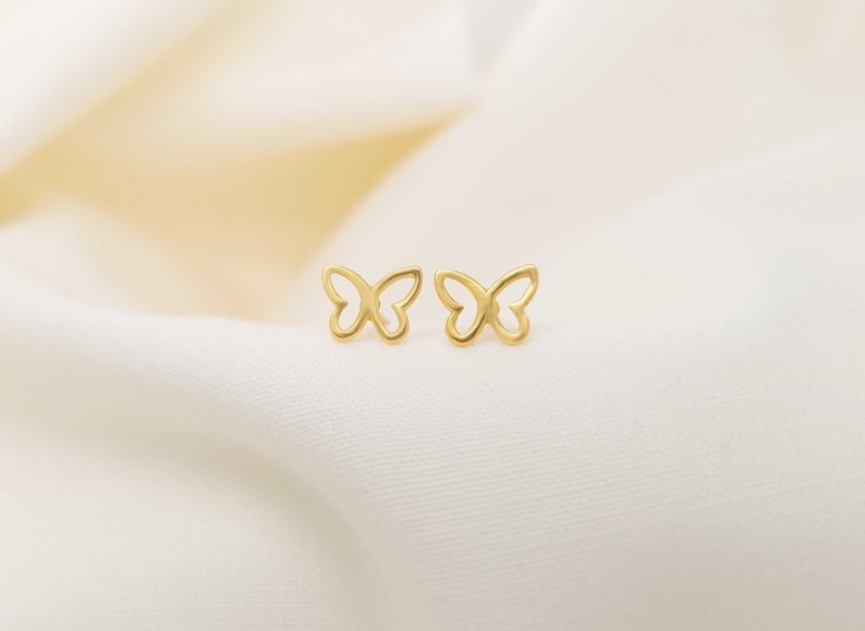 May include: A pair of gold butterfly stud earrings. The earrings are small and delicate, with a simple design.