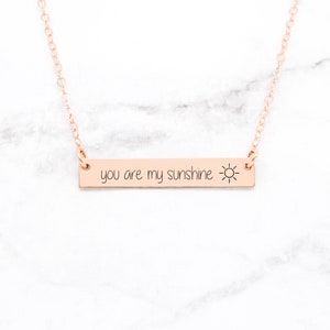 以下が含まれることがあります： 太陽のアイコンが付いた「you are my sunshine」と書かれたバーペンダントが付いた、ローズゴールドのネックレスです。