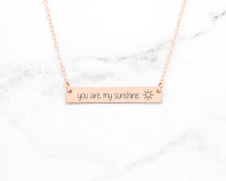 以下が含まれることがあります： 太陽のアイコンが付いた「you are my sunshine」と書かれたバーペンダントが付いた、ローズゴールドのネックレスです。