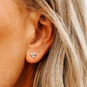 May include: Silver stud earrings with three small round beads in a triangular shape.