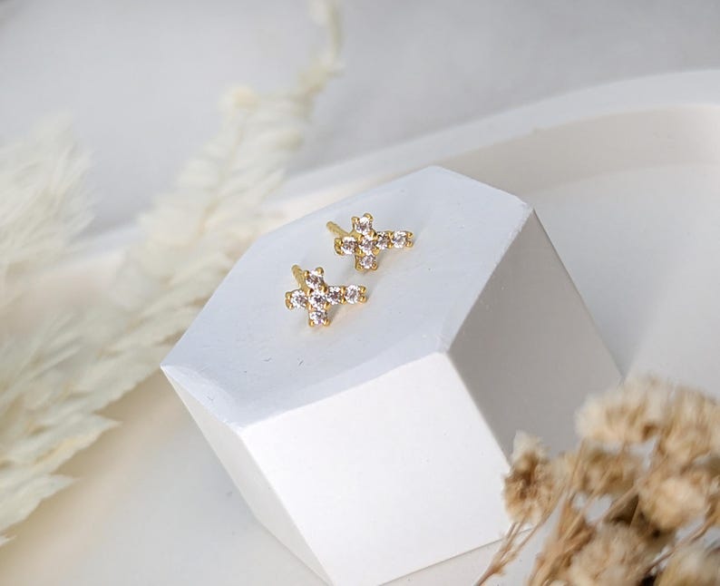 May include: A pair of gold cross earrings with clear cubic zirconia stones.