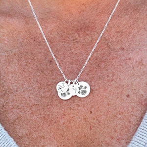 May include: A silver necklace with three charms. The charms are round and have a paw print and the letter "R" engraved on them.