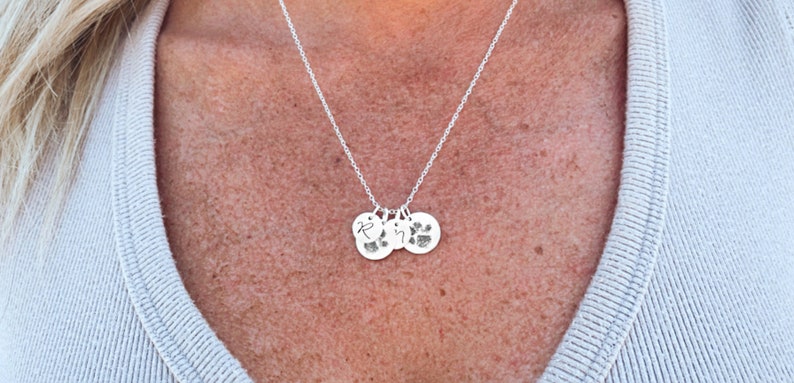 May include: A silver necklace with three charms. The charms are round and have a paw print and the letter "R" engraved on them.