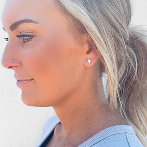 May include: A close-up of a person wearing small silver cross earrings. The person has blonde hair pulled back in a ponytail.
