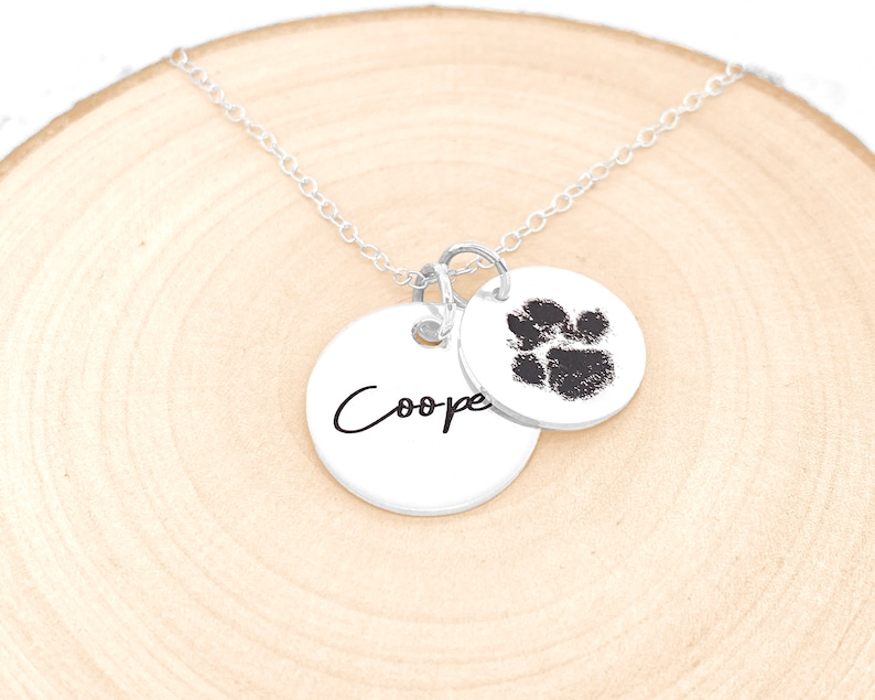 May include: Silver necklace with two charms. One charm is a paw print and the other charm has the name "Cooper" engraved on it.