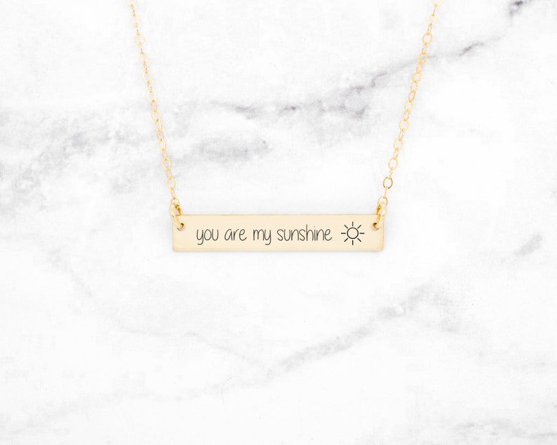 以下が含まれることがあります： 「you are my sunshine」という刻印と小さな太陽のアイコンが付いたゴールドバーネックレス
