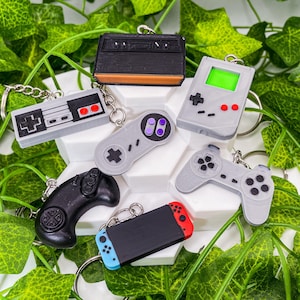 Puede incluir: Un conjunto de seis llaveros diferentes con forma de mandos de videojuegos. Los llaveros están hechos de plástico y presentan diferentes colores y diseños. Los llaveros incluyen un mando de Nintendo Entertainment System, un mando de Super Nintendo Entertainment System, una Game Boy Color, un mando de PlayStation, una Nintendo Switch y una consola Atari vintage.