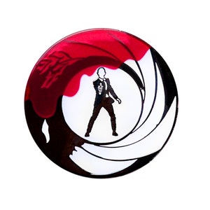 May include: A round, glossy, decorative item with a red and black design. A black silhouette of a person in a suit holding a gun is in the center. The design is reminiscent of a film's opening sequence.