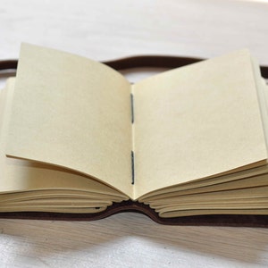 May include: A brown leather-bound journal with blank pages, open to reveal the cream-colored paper inside.