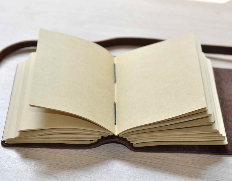 May include: A brown leather-bound journal with blank pages, open to reveal the cream-colored paper inside.