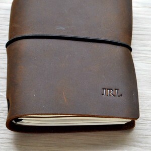 May include: A brown leather journal with a black elastic band closure and the initials "JRL" embossed on the front cover.