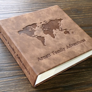 May include: A brown leather photo album with an embossed world map and the text "Arnett Family Adventures".