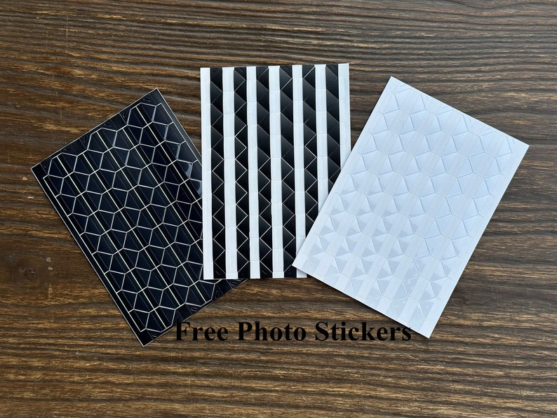 May include: Three sheets of photo corner stickers. One sheet has a black and white striped pattern, one sheet has a black honeycomb pattern, and one sheet has a white diamond pattern. Free Photo Stickers.