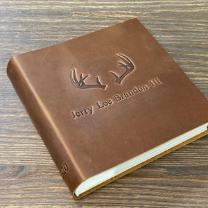 May include: A brown leather-bound journal with a personalised inscription that reads "Jerry Lee Brandon III" and a pair of stylised antlers above the name.
