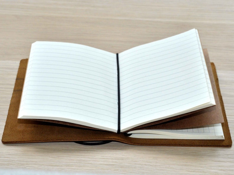 Może przedstawiać: Brązowy notes w sk&oacute;rzanej oprawie z czarną gumką. Notes jest otwarty, ukazując linie na stronach.