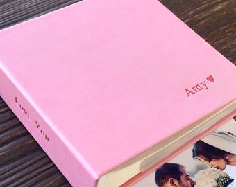 May include: A pink photo album with the words "Love You" embossed on the side and "Amy" with a heart symbol on the front. A wedding photo is visible inside the album.