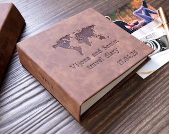 Könnte beinhalten: Braunes Leder-Reisetagebuch mit einer geprägten Weltkarte auf dem Einband. Das Tagebuch ist personalisiert mit den Namen "Vijona und Samet" und dem Text "Reisetagebuch 17.04.25".