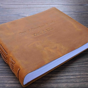 Op de afbeelding: Een bruin lederen gebonden dagboek met de tekst "Our Adventure Book Zach & Ella" gegraveerd op de voorzijde.