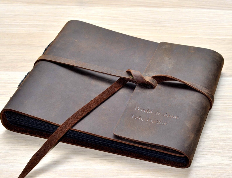 May include: A brown leather photo album with a tied closure and personalized inscription: "David & Anna Feb. 14, 2017".