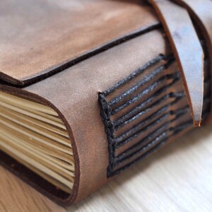 May include: A brown leather-bound journal with black stitching and a leather strap closure. The journal has a rustic and vintage aesthetic.