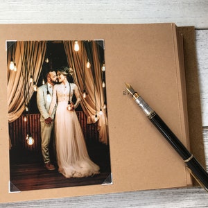 May include: A brown leather-bound photo album with a white photo of a couple kissing under a string of lights. The photo is framed with a white border.