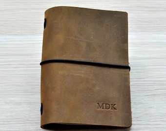 May include: A brown leather notebook with an elastic band closure and the initials "MDK" embossed on the front.