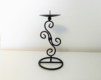 May include: Black wrought iron candle holder with a circular base and a decorative, swirling design. The candle holder has a small, round platform to hold a candle. The design is elegant and suitable for home decor.