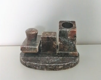 Op de afbeelding: Een vintage bureauset gemaakt van gevlekte bruine steen. De set bevat een stempel, een kleine doos en een penhouder, allemaal gemonteerd op een afgeronde basis. De steen heeft een natuurlijke, verouderde uitstraling, met variaties in kleur en textuur.