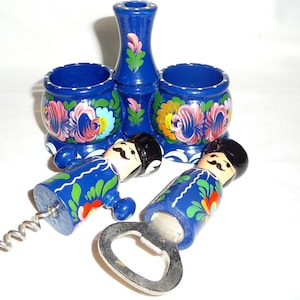 Può includere: Un set di sale e pepe in legno dipinto di blu e bianco con un apribottiglie e un cavatappi abbinati. I salieri hanno disegni floreali e l'apribottiglie e il cavatappi hanno la forma di persone.