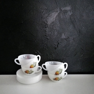 May include: A collection of vintage white teacups and saucers. The teacups feature a diagonal design and a painted image of a yellow fruit with green leaves. The teacups are stacked, with a stack of saucers beneath them.