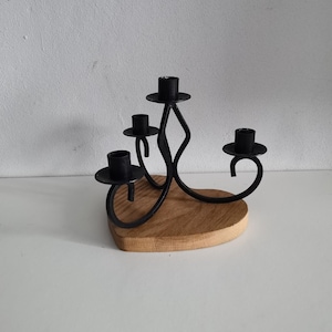 Puede incluir: Candelero de metal negro con cuatro portavelas, con un diseño decorativo de espiral. El candelero está montado sobre una base de madera.