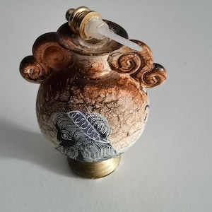 Può includere: Piccola bottiglia decorativa in ceramica con un design dettagliato. La bottiglia ha una combinazione di colori marrone e crema, con una base e un tappo dorati. Presenta una texture screpolata dettagliata e un design decorativo.