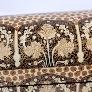 May include: Close-up of a decorative box with intricate floral patterns. The design features beige leaves and white floral accents against a black background. The lid has a repeating pattern of brown circles.