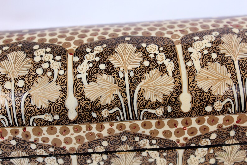 May include: Close-up of a decorative box with intricate floral patterns. The design features beige leaves and white floral accents against a black background. The lid has a repeating pattern of brown circles.