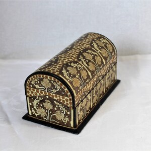 May include: A decorative, arched-top chest with a black base. The chest features a brown and tan floral pattern with a dotted design on the curved top. The edges are trimmed in black, creating a vintage aesthetic.