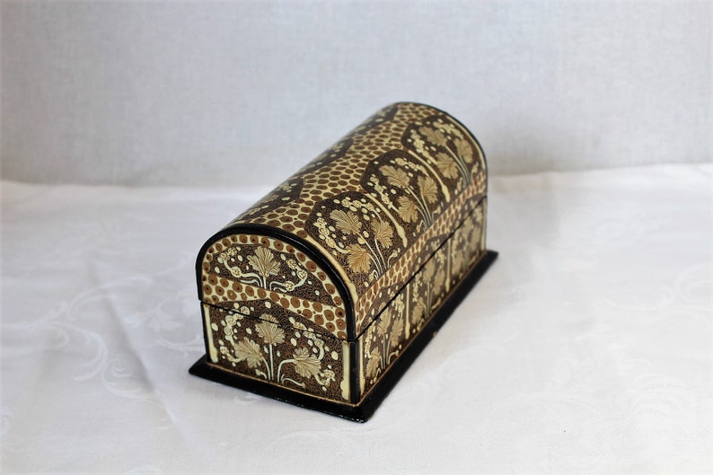 May include: A decorative, arched-top chest with a black base. The chest features a brown and tan floral pattern with a dotted design on the curved top. The edges are trimmed in black, creating a vintage aesthetic.