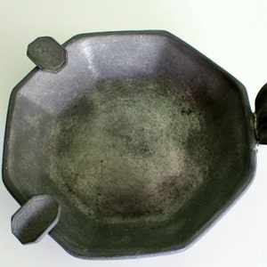May include: A pewter-toned, octagonal bowl with three decorative handles. The bowl has a textured surface and a shallow depth. The handles are stylized, with one resembling a leaf. The bowl is likely vintage and suitable for decorative use.