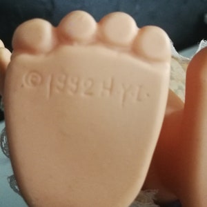 May include: Close-up of a doll's foot, showing the sole with the embossed text "&copy; 1992 H.Y.L.". The foot is a light peach colour, with visible toes. The doll's foot is in focus, with a blurred background.