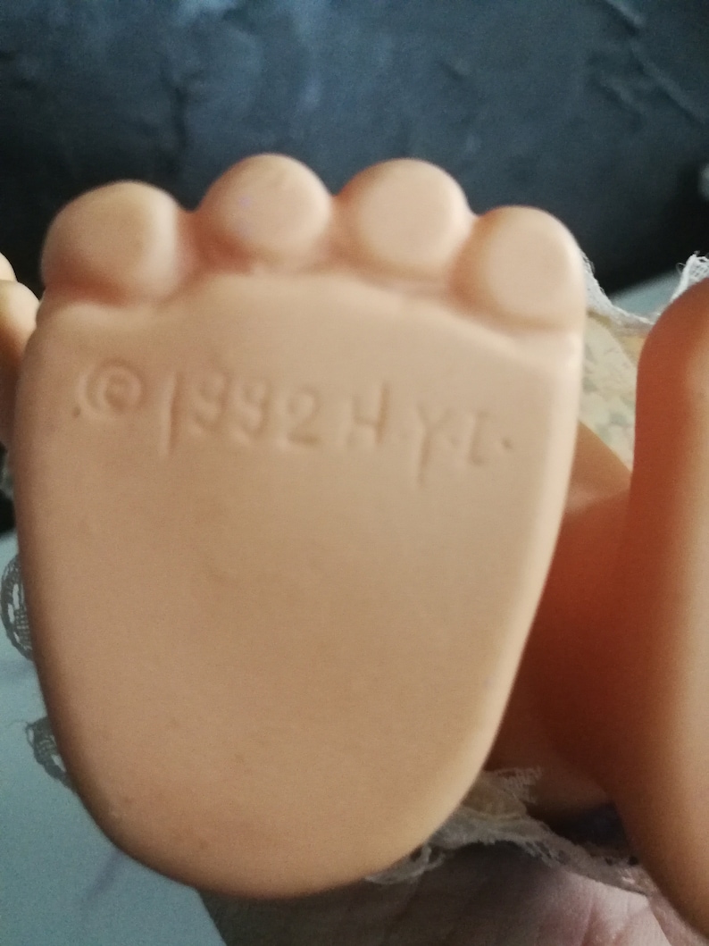 May include: Close-up of a doll's foot, showing the sole with the embossed text "&copy; 1992 H.Y.L.". The foot is a light peach colour, with visible toes. The doll's foot is in focus, with a blurred background.