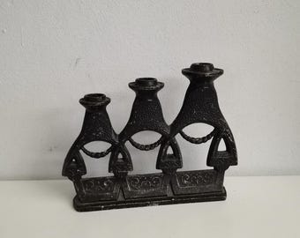 Puede incluir: Un candelero de metal negro con tres portavelas. El candelero tiene un diseño decorativo con un patrón repetitivo de círculos y líneas.