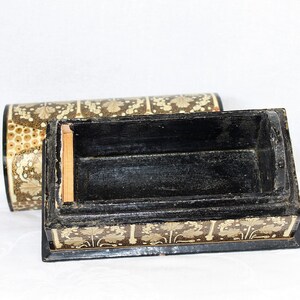 May include: An open, rectangular black box with a matching lid. The box and lid are decorated with a repeating pattern of gold-colored floral designs on a dark brown background. The interior of the box is black.