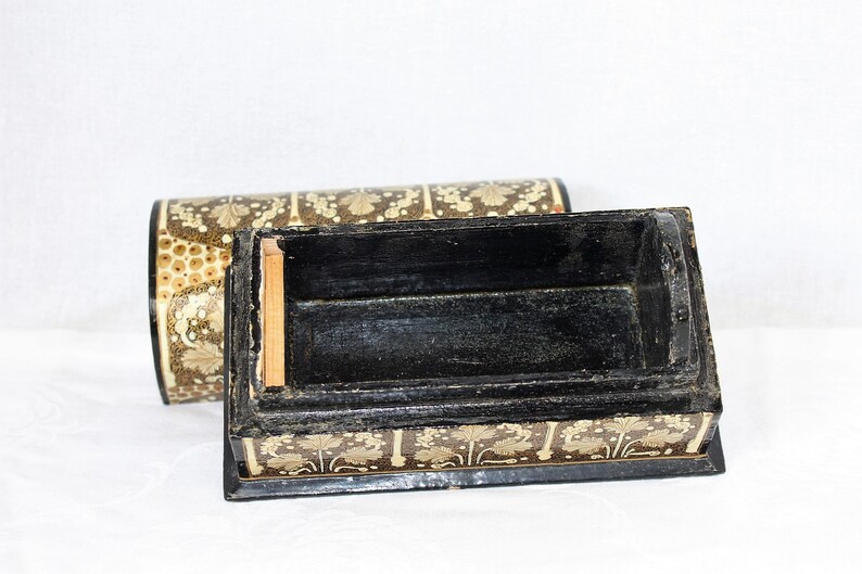 May include: An open, rectangular black box with a matching lid. The box and lid are decorated with a repeating pattern of gold-colored floral designs on a dark brown background. The interior of the box is black.