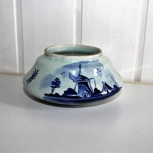 May include: A ceramic bowl with a light blue exterior and a dark blue windmill scene. The bowl has a wide, shallow shape with a slightly flared rim. The windmill scene includes trees and other landscape elements.