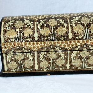 May include: A decorative, arched-top box with a black base and lid. The box is adorned with a repeating pattern of stylized leaves in cream and gold against a dark brown background. The design includes small, circular accents.